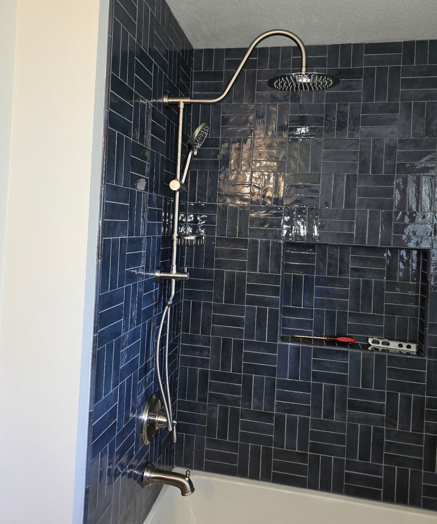 Bathtub and rainfall shower with dark blue tile surround